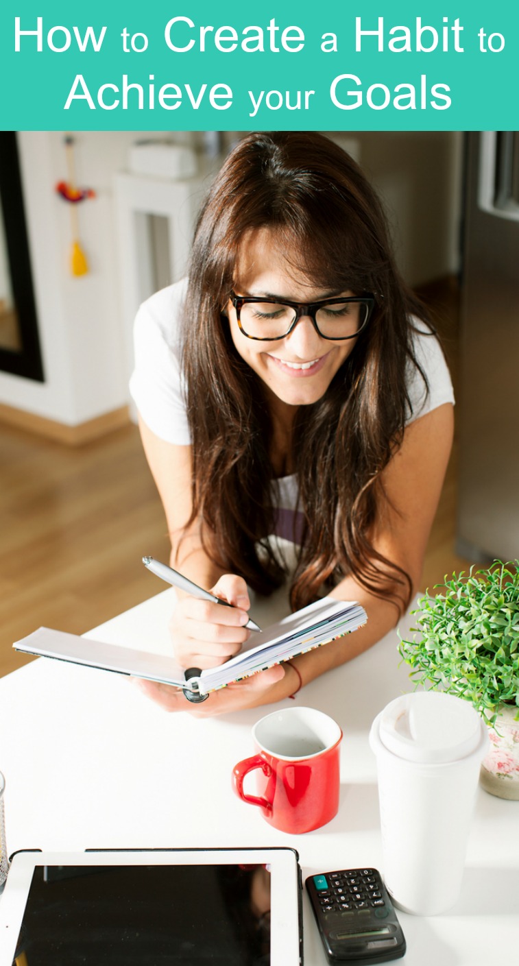 A brunette woman learning how to a create a habit to achieve her goals at her desk writing in her planner with coffee and an ipad on her desk in front of her.