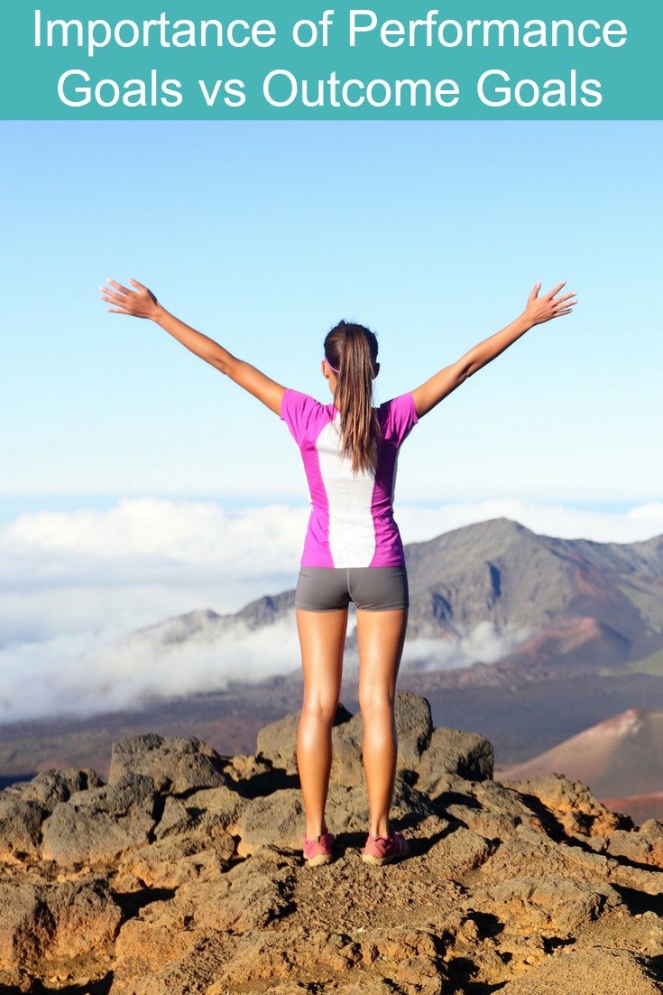 A woman standing on top of mountain with her arms up in triumphant from hitting her performance goals